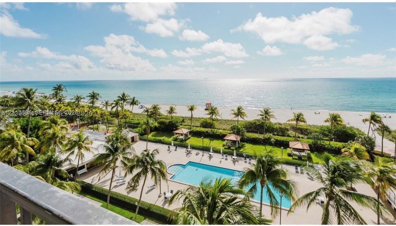 Outdoor pool area featuring a paved deck, mature palm trees, shaded cabanas, and direct beach access
