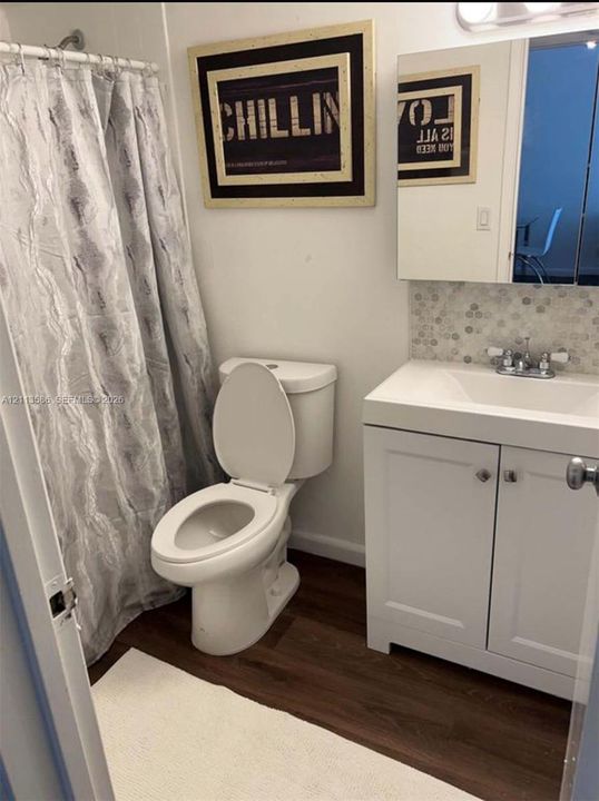Bathroom featuring a white vanity cabinet with a stone-top integrated sink, mosaic tile backsplash, wood-finish flooring, and a mirrored medicine cabinet