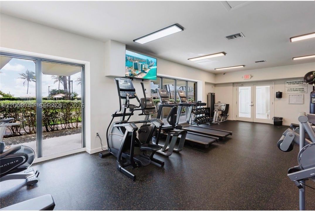 Fitness center featuring resilient rubber flooring, expansive floor-to-ceiling glass panel walls, and recessed surface-mount lighting
