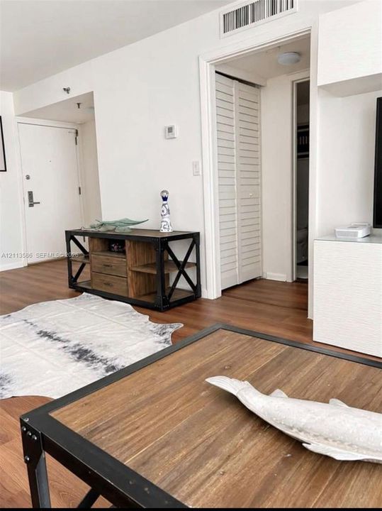 Living area featuring wood-finish flooring, crisp white walls, and built-in closet storage with louvered doors