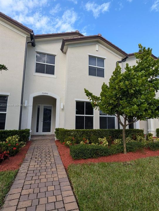 Stucco exterior featuring an arched entryway, double glass-paneled front doors, a paver walkway, and manicured shrubbery
