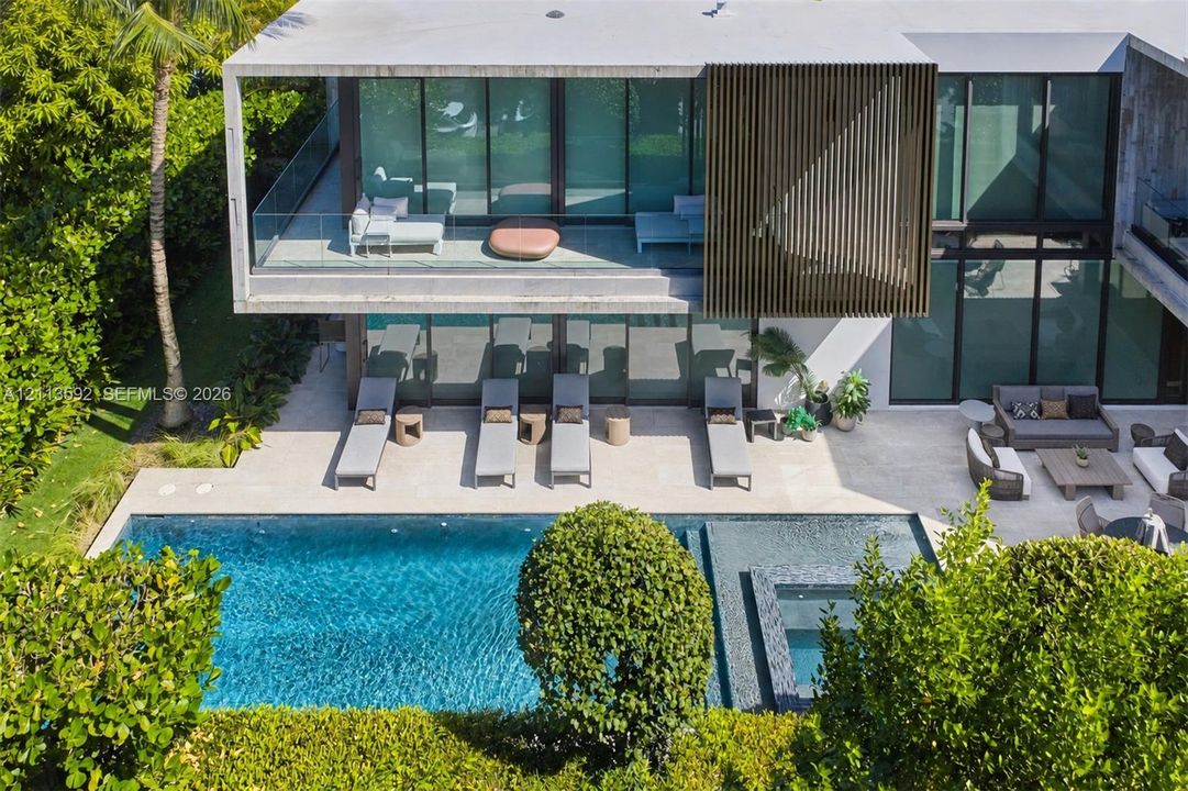 Modern concrete exterior featuring floor-to-ceiling glass walls, a cantilevered second-story balcony with glass railing, vertical wood-slat privacy screening, and a swimming pool with integrated spa