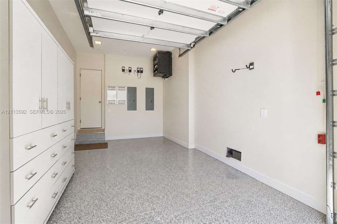 Garage interior featuring white built-in cabinetry, durable speckled epoxy flooring, overhead storage unit, and recessed lighting