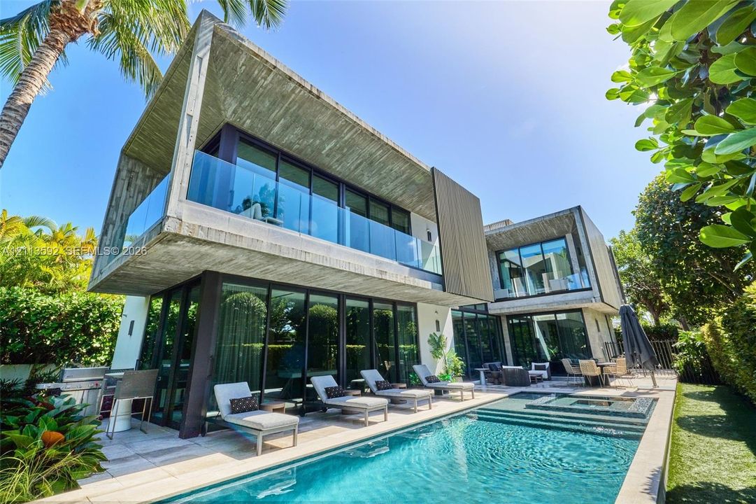 Modern architectural exterior featuring exposed concrete construction, floor-to-ceiling glass paneling, glass balcony railings, and a private swimming pool with integrated spa