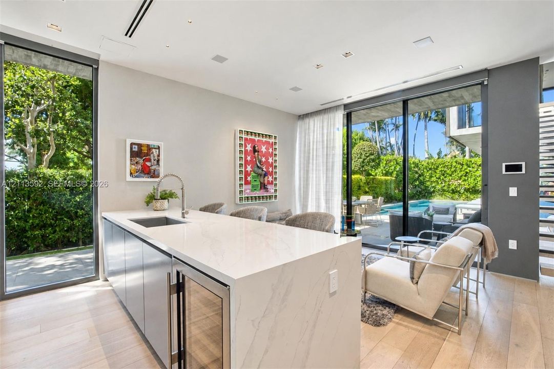 Kitchen island featuring a waterfall stone countertop, integrated beverage refrigerator, under-mount sink, and gooseneck faucet, complemented by wood-finish flooring and floor-to-ceiling sliding glass doors