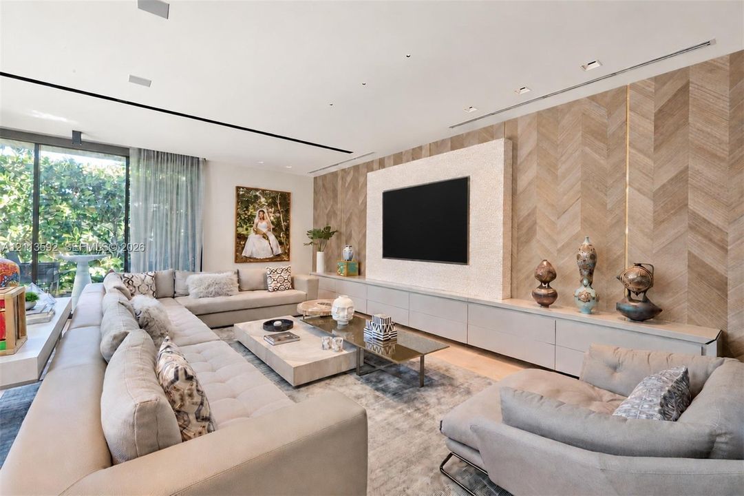 Living room featuring a floor-to-ceiling herringbone wood-paneled accent wall, built-in floor-level cabinetry with a stone-textured central hearth, recessed ceiling lighting, and large floor-to-ceiling sliding glass panels