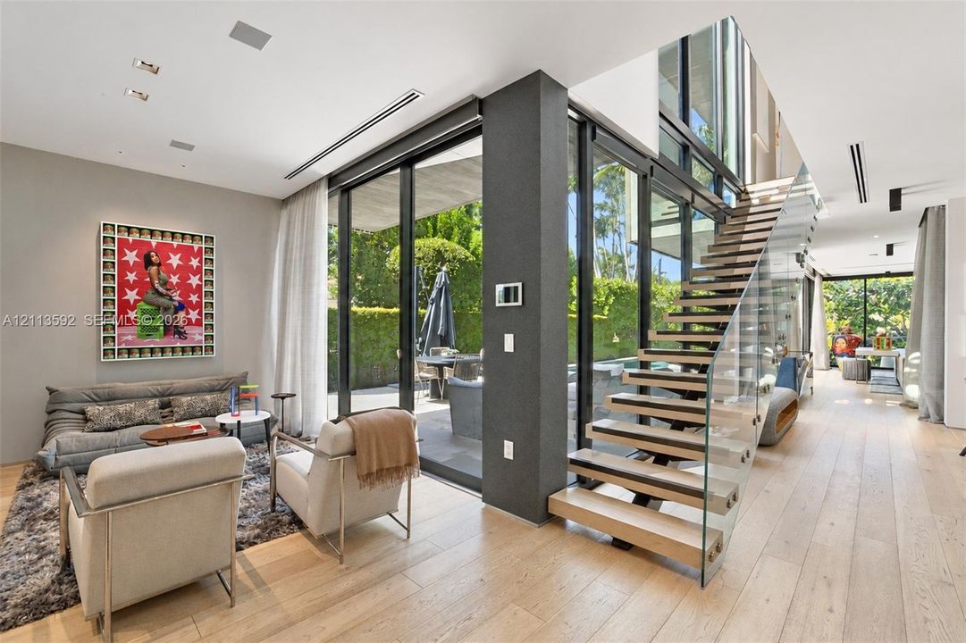 Open-concept living space featuring wood-finish flooring, floor-to-ceiling glass walls, and a floating staircase with glass balustrades