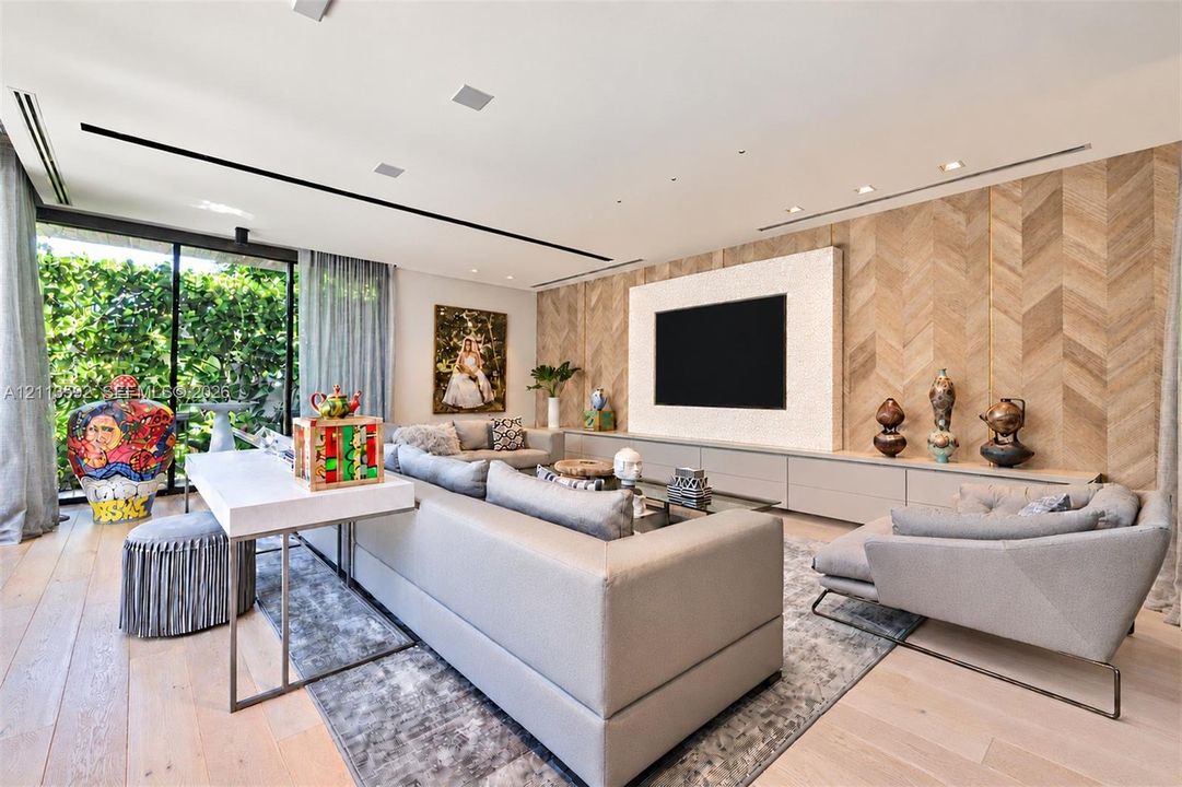 Living area featuring wood-finish flooring, herringbone-patterned wood wall paneling, floor-to-ceiling glass sliding doors, recessed linear lighting, and built-in handleless cabinetry