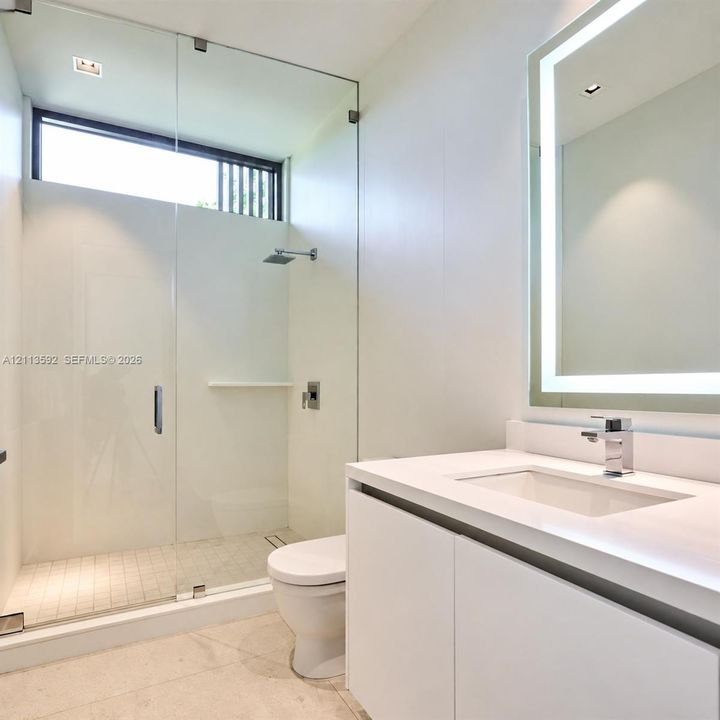 Modern bathroom featuring a glass-enclosed shower with a rainfall showerhead, a floating vanity with an integrated rectangular sink, a polished chrome faucet, and a large backlit wall mirror