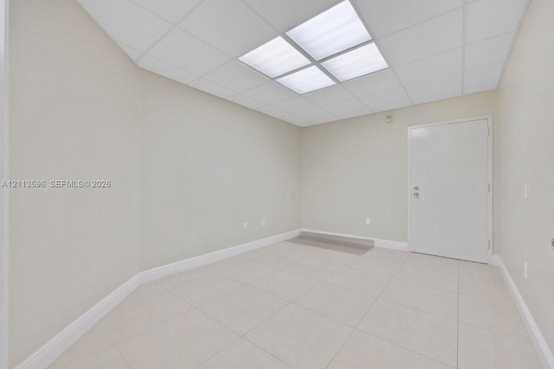 Neutral-toned room featuring large-format tile flooring, a drop ceiling with recessed lighting, and a solid-core interior door
