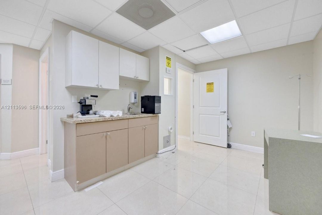 Built-in cabinetry with stone-finish countertops, undermount sink, suspended ceiling panels, and tile flooring