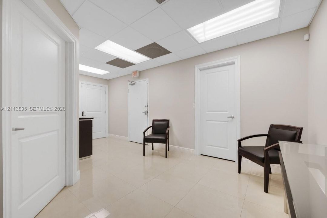 Neutral-toned interior featuring large-format tile flooring, drop ceiling with recessed panel lighting, and three solid-core interior doors