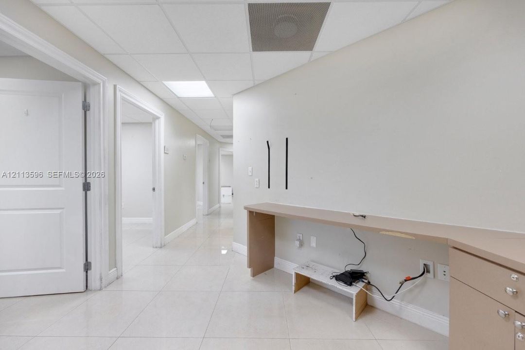Interior hallway featuring light-colored tile flooring, drop ceiling panels with recessed lighting, and a built-in laminate desk with integrated cabinetry