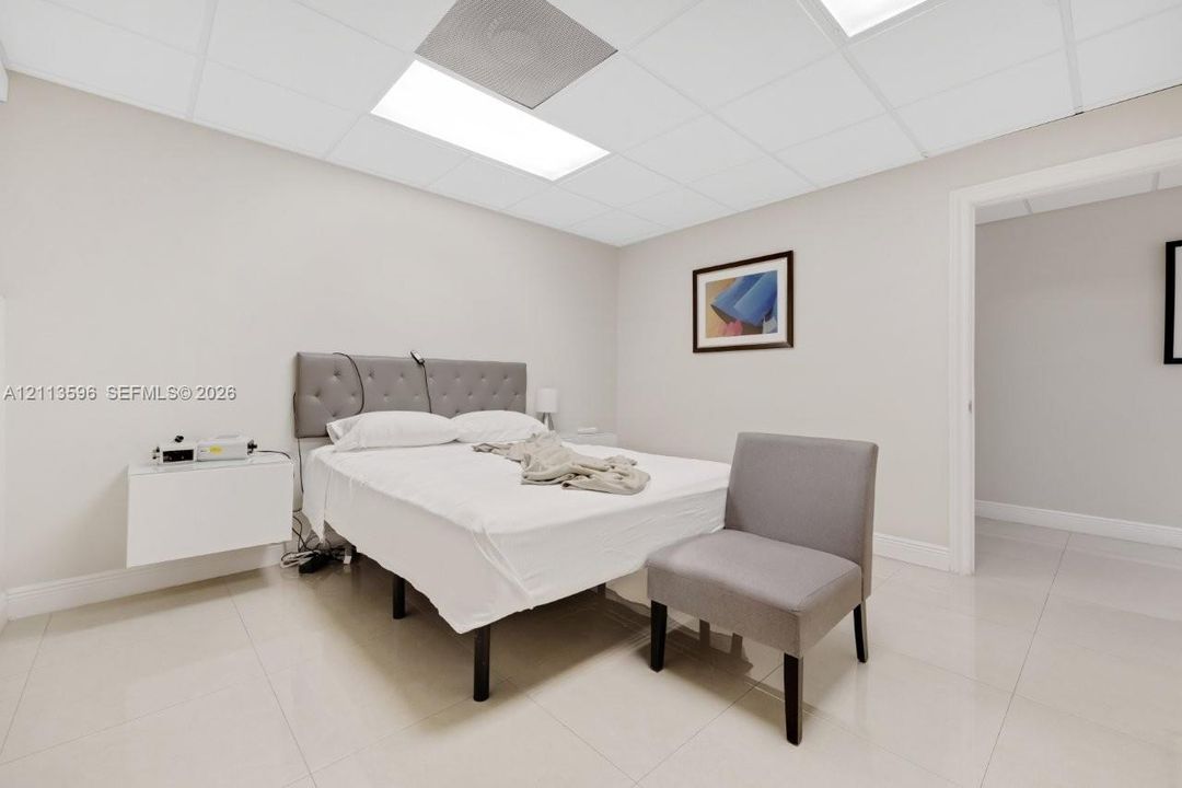 Neutral-toned room featuring large-format tile flooring, a suspended wall-mounted cabinet, and a drop ceiling with recessed lighting