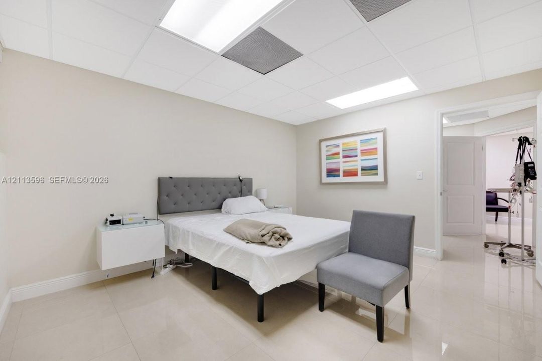 Neutral-toned interior space featuring light-colored tile flooring, recessed grid ceiling panels, and a wall-mounted white cabinetry unit