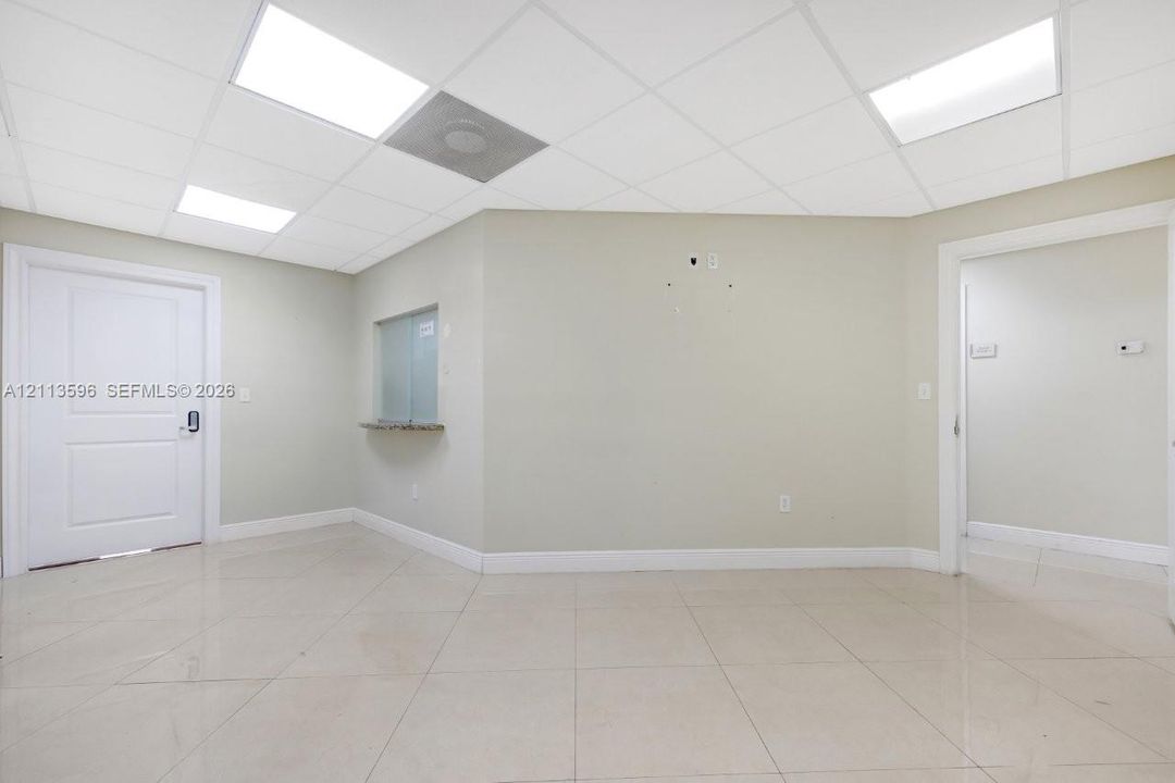 Interior space featuring large-format tile flooring, drop ceiling with recessed panel lighting, neutral painted walls, and a service window with a stone-finish counter