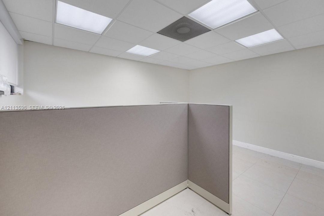 Interior space featuring neutral-toned walls, tile flooring, built-in fabric-paneled partitions, and a drop ceiling with recessed lighting panels