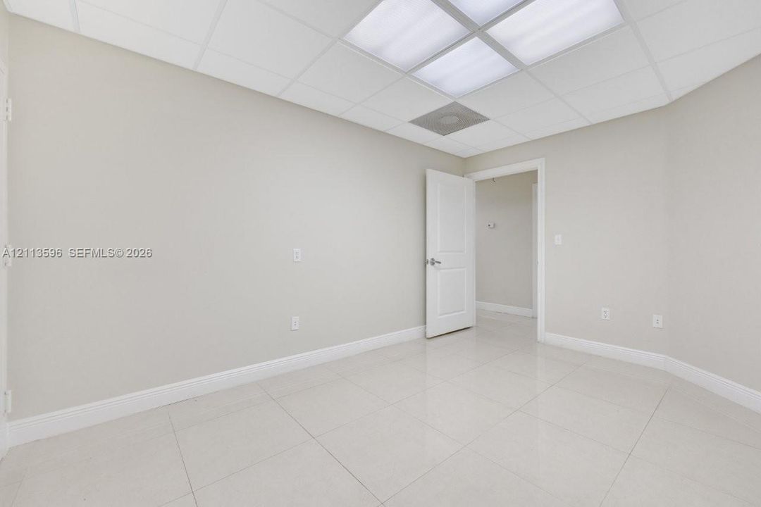 Room featuring large-format tile flooring, drop ceiling with integrated panel lighting, and a solid-core interior door