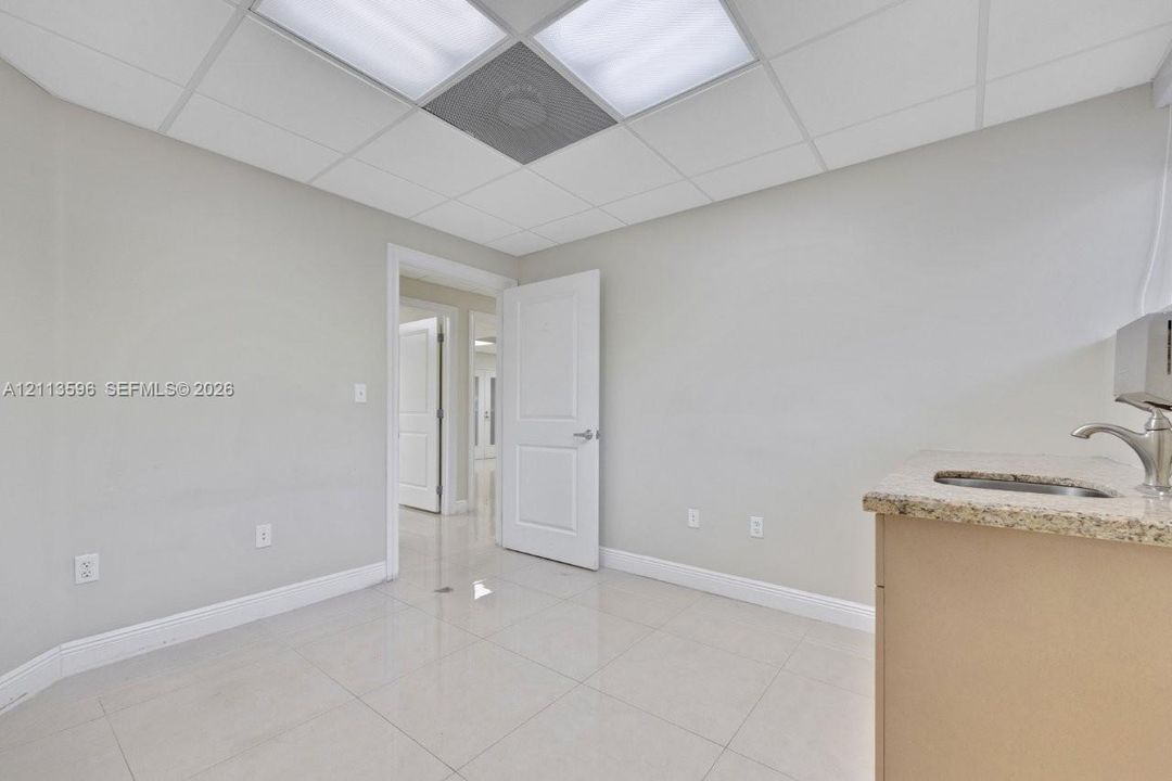 Interior space featuring light-colored tile flooring, drop ceiling with integrated panel lighting, and a built-in cabinet with stone-finish countertop and undermount sink