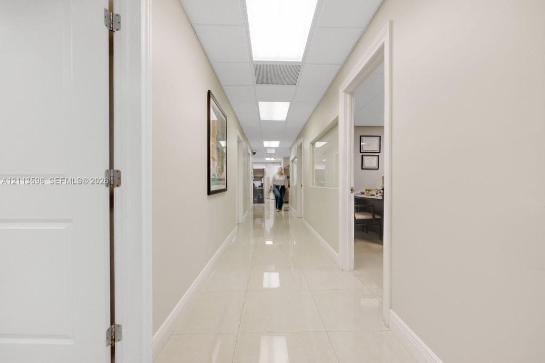 Interior hallway featuring polished tile flooring, drop ceiling with integrated recessed lighting, and interior walls with inset glass paneling