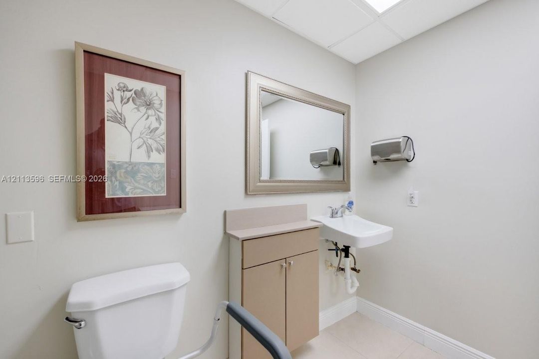 Wall-mounted ceramic sink, neutral-toned cabinetry with solid-surface countertop, framed wall mirror, and integrated safety rail