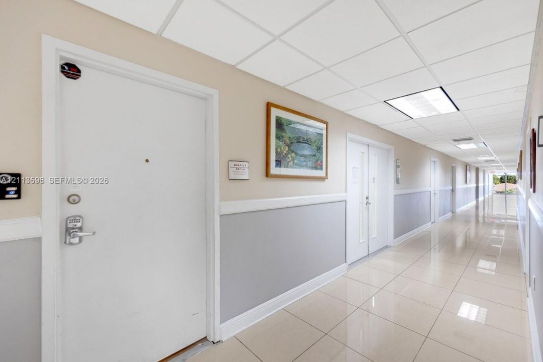 Interior hallway featuring neutral two-tone wall paint, ceramic tile flooring, and drop-ceiling panels with recessed lighting