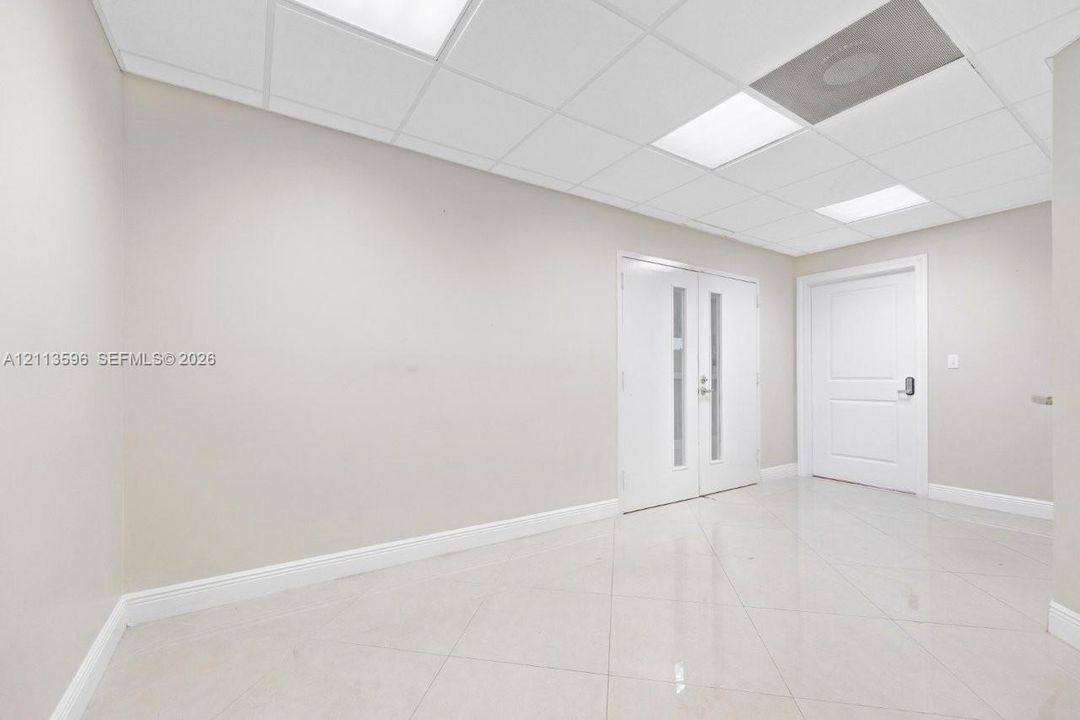 Spacious interior featuring large-format tile flooring, a suspended drop ceiling with recessed lighting, double doors with vertical glass inserts, and a solid-core panel door