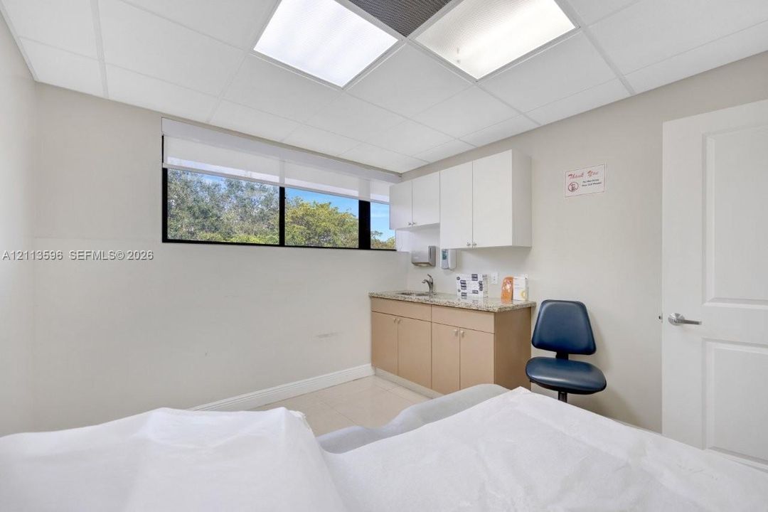 Drop ceiling with recessed lighting, integrated cabinetry with stone-finish countertop, stainless steel sink, tile flooring, and horizontal window