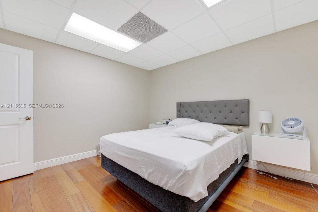 Room featuring wood-finish flooring, drop ceiling with integrated recessed lighting, and a solid-core interior door