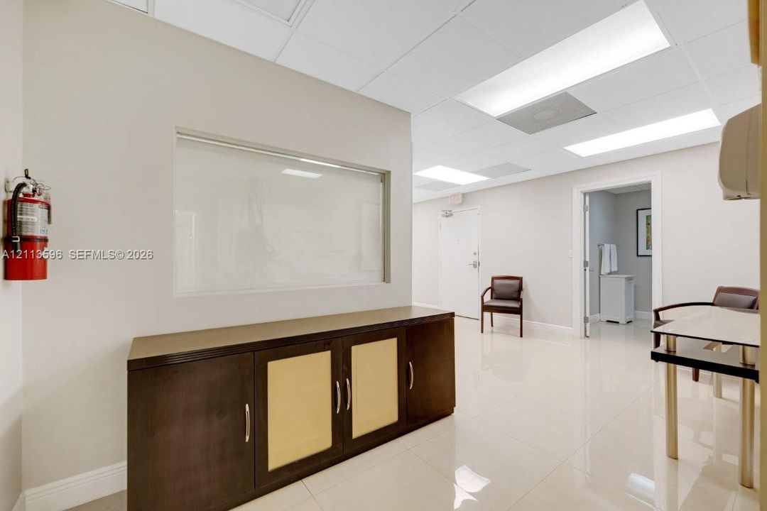 Interior space featuring neutral wall paint, polished tile flooring, a drop ceiling with recessed lighting, and a built-in cabinetry unit with glass partition