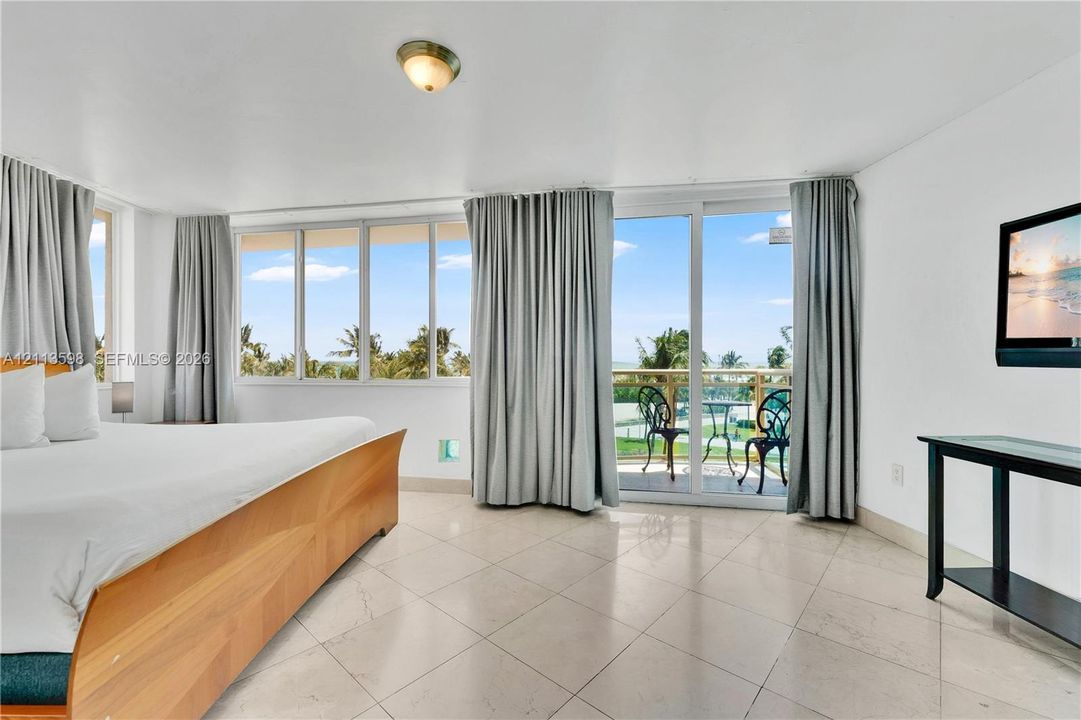 Large-format windows, sliding glass door with access to a balcony, light-toned stone-finish tile flooring, and a flush-mount ceiling light fixture