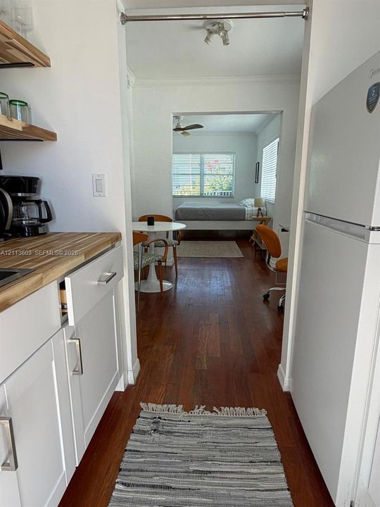 Kitchen featuring white shaker-style cabinetry, wood-finish countertops, and open wood shelving, complemented by wood-finish flooring throughout the unit
