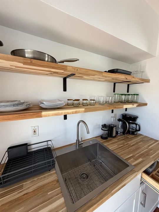 Butcher block countertop, stainless steel undermount sink, arched high-arc faucet, and dual-tier wood shelving with matte black metal brackets