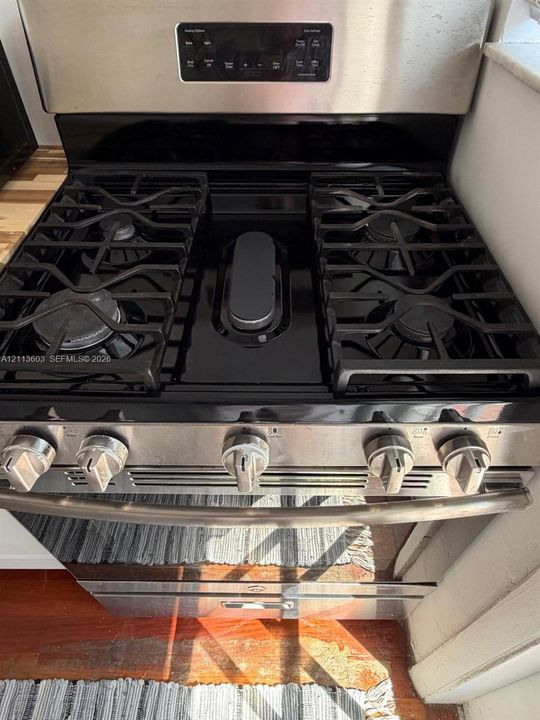 Stainless steel gas range featuring four burners, a central griddle, and a built-in control panel