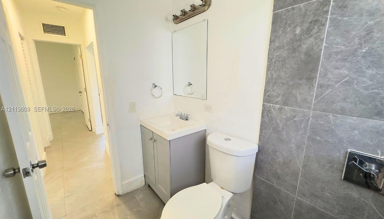 Bathroom featuring a grey vanity cabinet with a white integrated sink, polished chrome fixtures, a rectangular wall-mounted mirror, and stone-finish wall tile