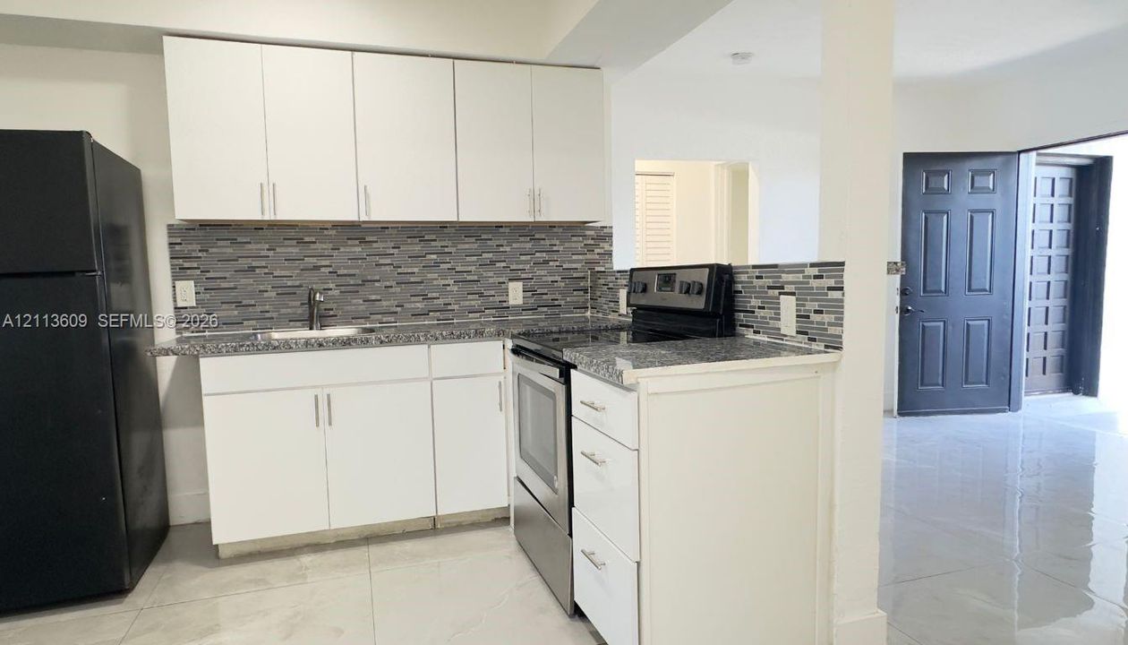 Kitchen featuring white shaker-style cabinetry, stone-finish countertops, decorative multi-tonal tile backsplash, and stainless steel appliances