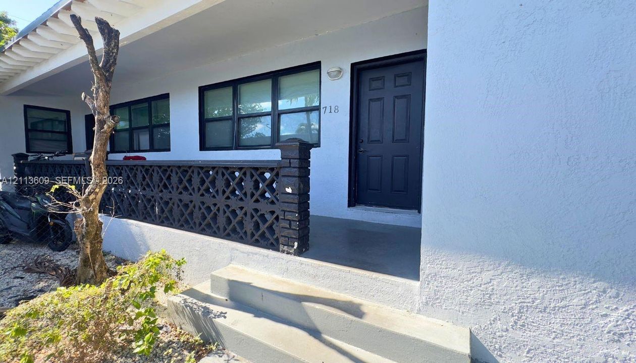 Exterior entryway featuring a white stucco facade, black paneled front door, concrete steps, and decorative masonry railing
