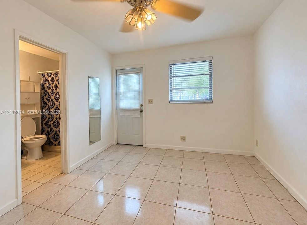 Interior space featuring light-colored tile flooring, a ceiling fan with integrated lighting, a flush-mounted wall mirror, and an exterior door with a window insert