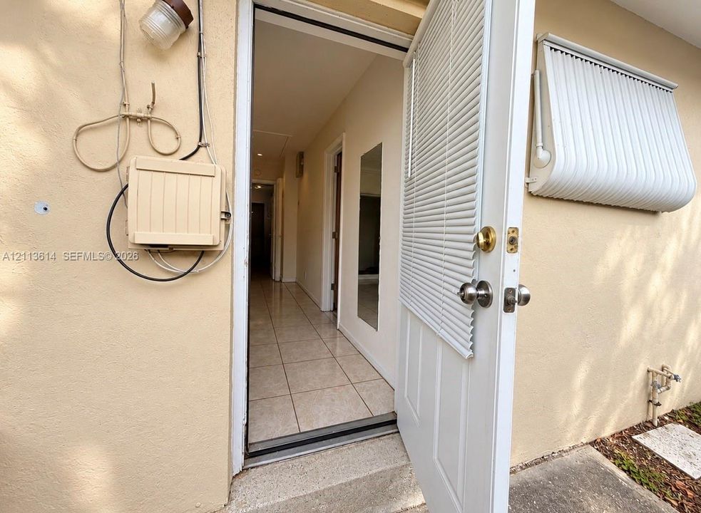 Exterior entry featuring an integrated door blind, a metal window awning, and tile flooring