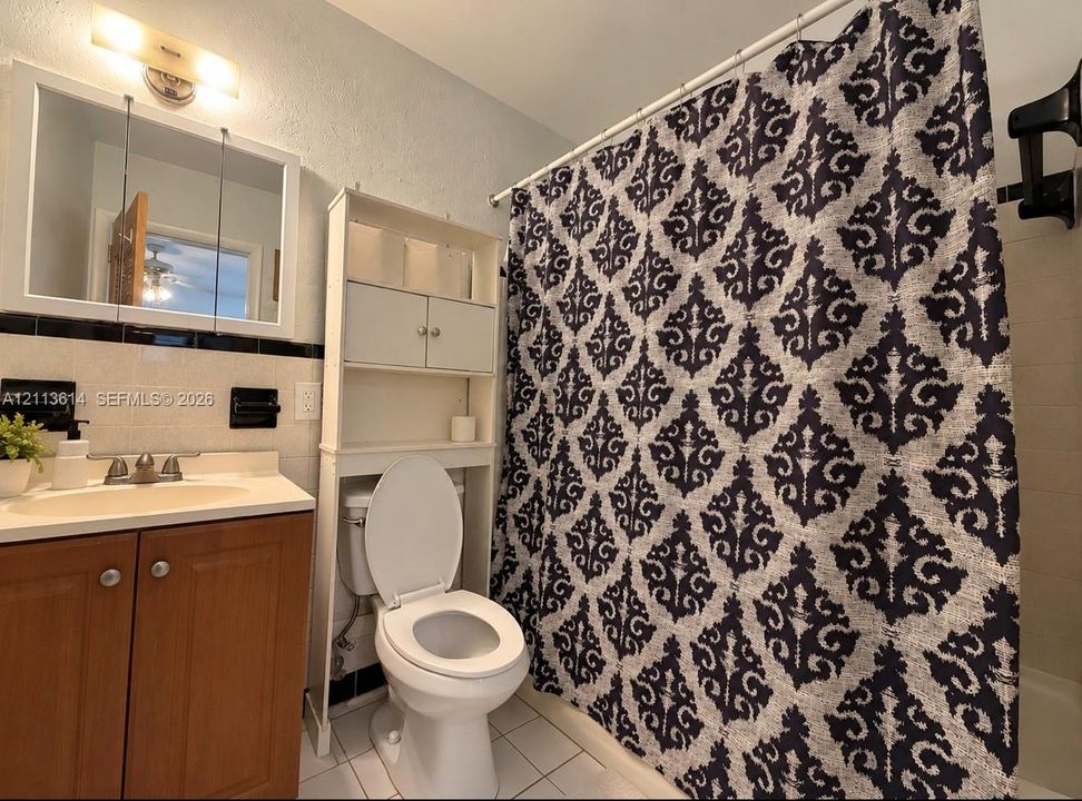 Bathroom featuring a wood-finish vanity, solid-surface countertop, medicine cabinet, tile wall accent with black trim, and white floor tiling