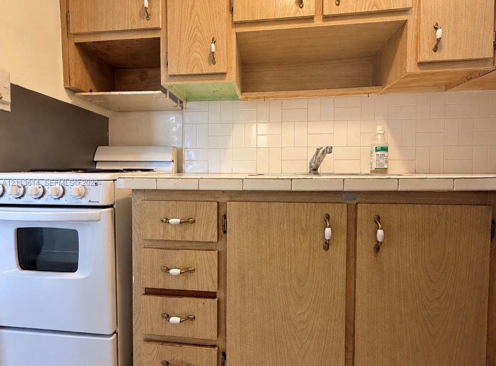 Kitchen area featuring wood-finish cabinetry, tile backsplash, tile countertop, integrated sink with faucet, and built-in gas range