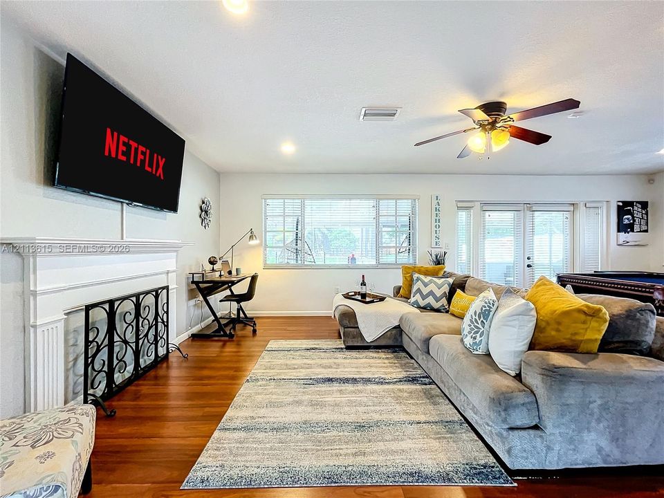 Living area featuring wood-finish flooring, a white mantel fireplace, a ceiling fan, and multi-pane windows
