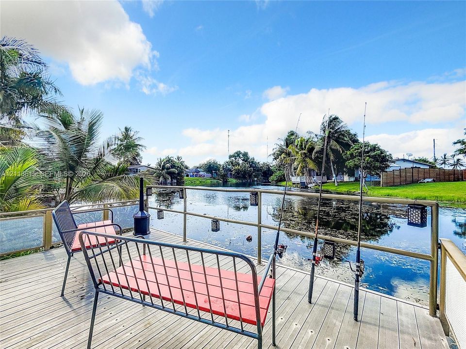Waterfront wooden deck featuring built-in metal railing, hanging light fixtures, and direct water access