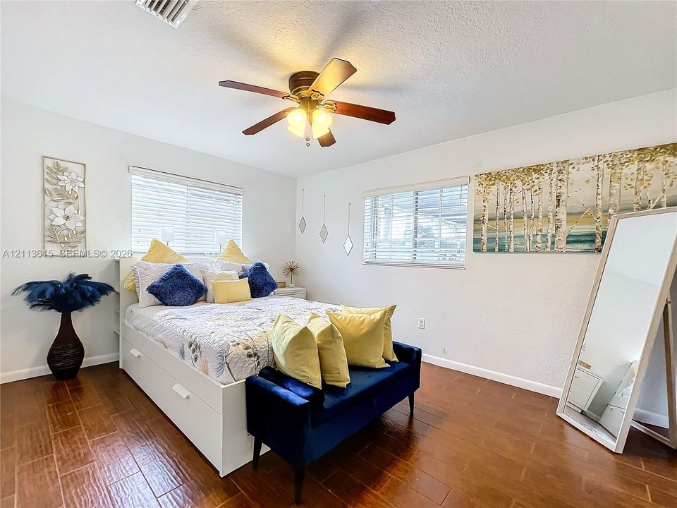 Wood-finish flooring, dual windows with horizontal blinds, and a central ceiling fan with integrated lighting