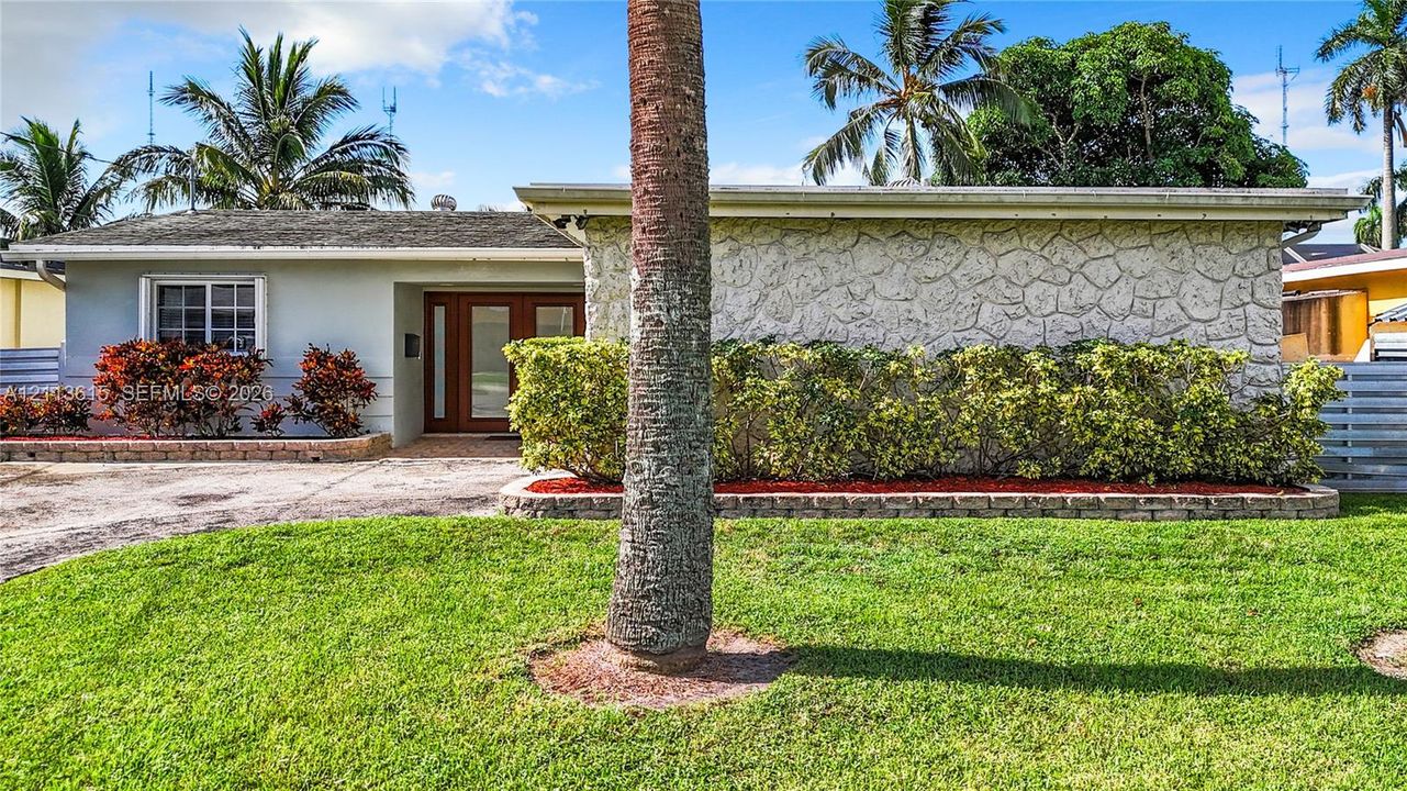 Single-story residence featuring a textured stone facade, wood-framed glass-panel entry door, and manicured landscaping with mature palm trees