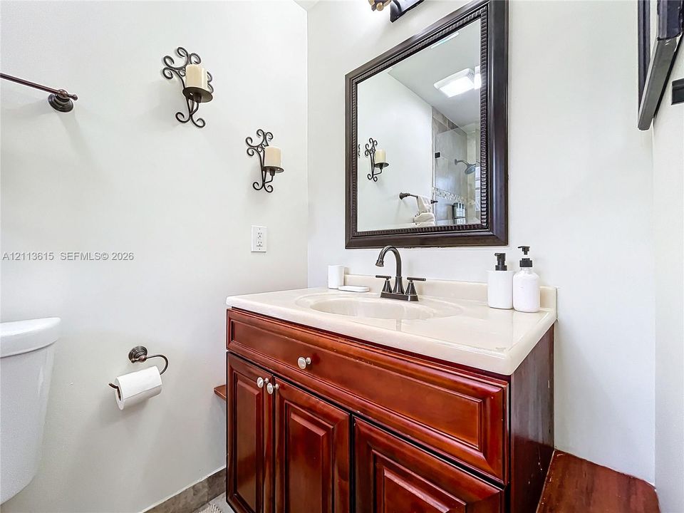 Dark-stained wood cabinetry, integrated basin countertop, wall-mounted bronze-finish faucet, framed mirror, and decorative wall-mounted lighting sconces