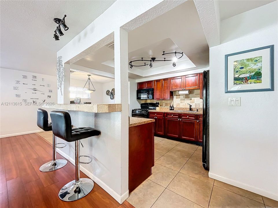 Kitchen featuring dark wood-finish cabinetry, stone-texture countertops, tile backsplash, built-in black appliances, and recessed track lighting