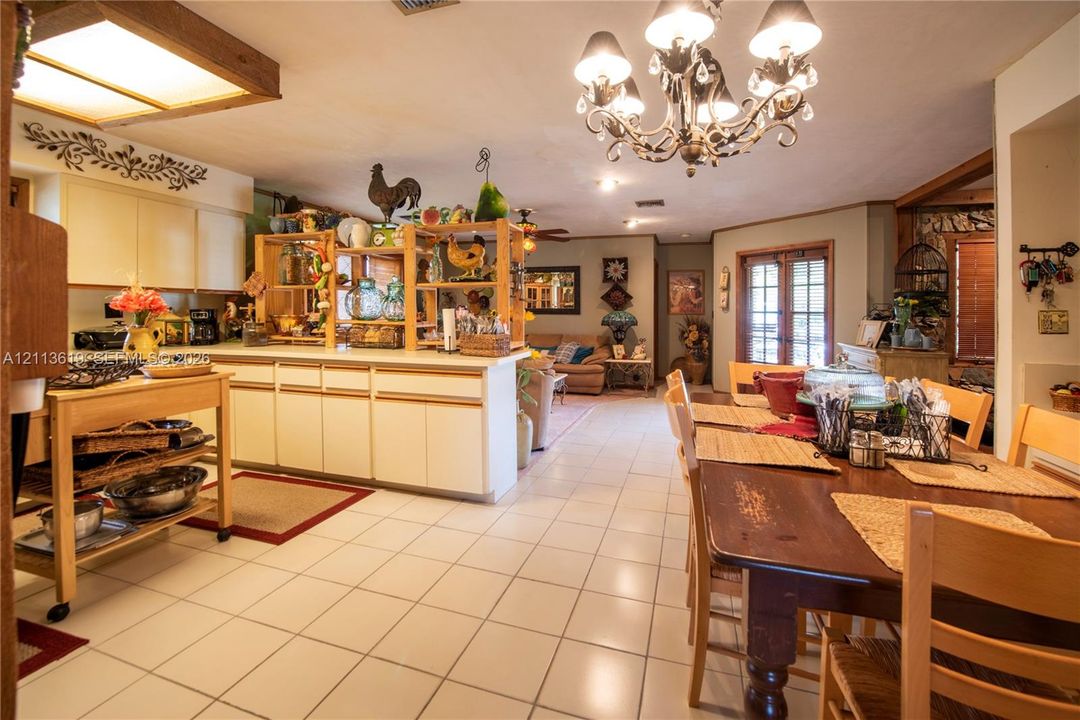 Open-concept kitchen featuring light-toned cabinetry, ceramic tile flooring, a multi-arm chandelier with decorative glass elements, and double-door access to exterior space
