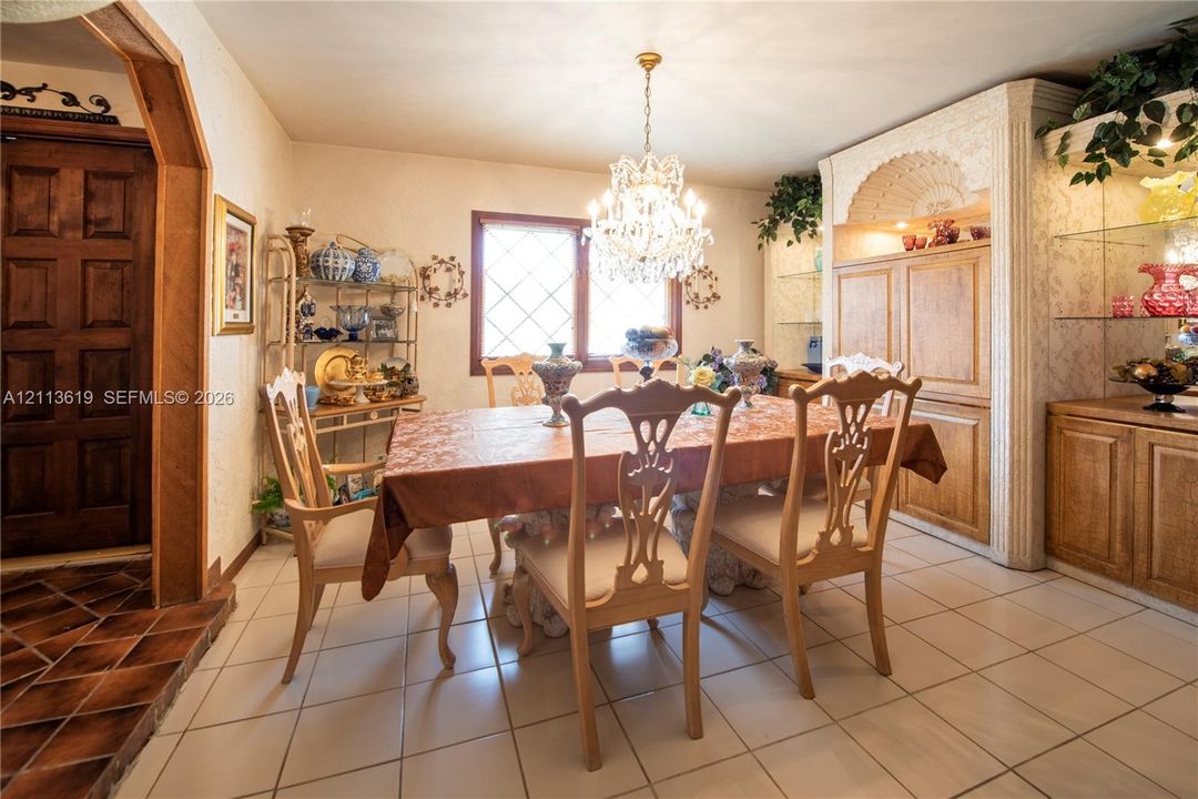 Dining area featuring tiled flooring, a crystal chandelier, arched wooden doorway, and built-in cabinetry with glass shelving