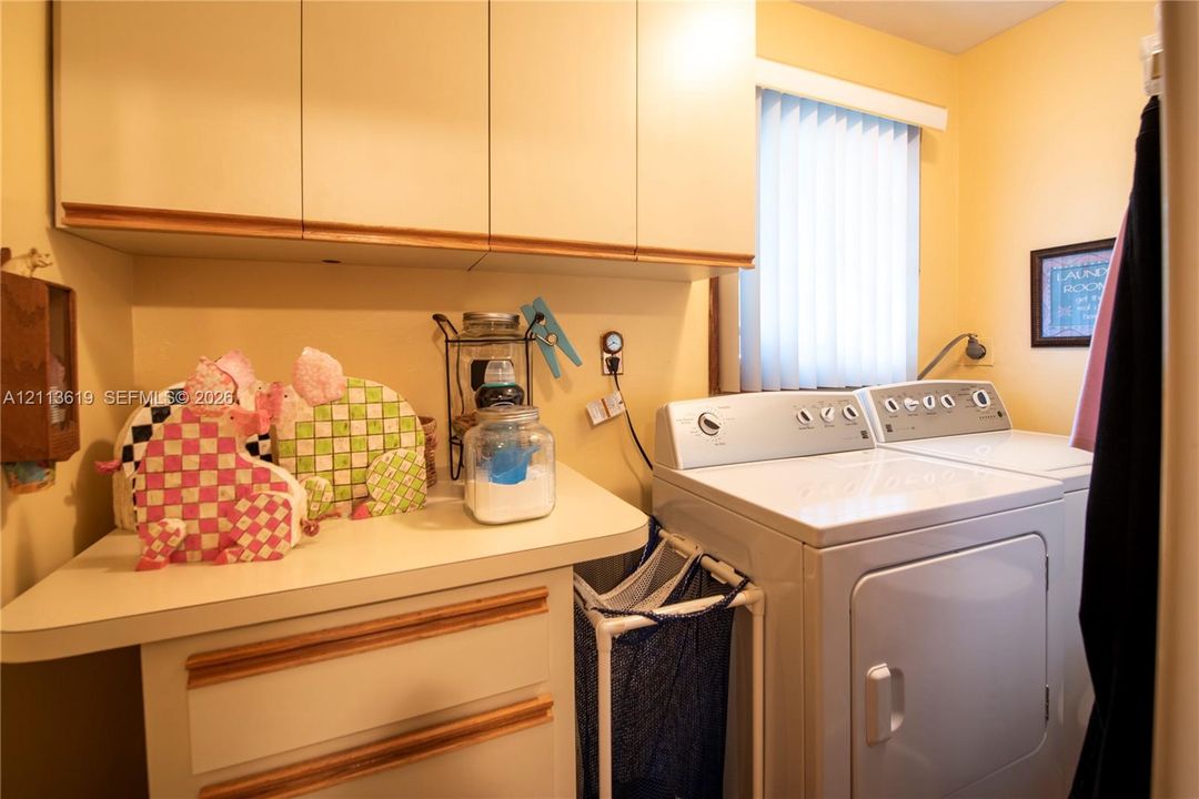Laundry area featuring ample solid-surface countertop space, extensive upper cabinetry, and vertical blind window treatments